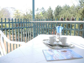 Ein Balkon mit Tisch für zwei Personen, einer blauen Kaffeekanne und einer Zeitschrift.