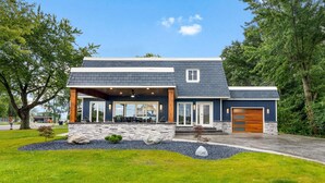 Une maison moderne avec une façade en pierre, un porche abrité et un grand garage.