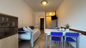 A compact room with a bed, a small kitchenette, a dining table with chairs, and a TV mounted on the wall. - Precious Flat 100mt From the Beach - Beahost (San Michele al Tagliamento)