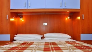 Una cama bien hecha con una manta escocesa, cabecera de madera y un interruptor de luz arriba.