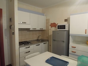A compact kitchen with white cabinets, a gas stove, a sink, a microwave, and a refrigerator.