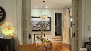 A room with a wooden floor, a desk with a lamp, a chair, and a painting on the wall.
