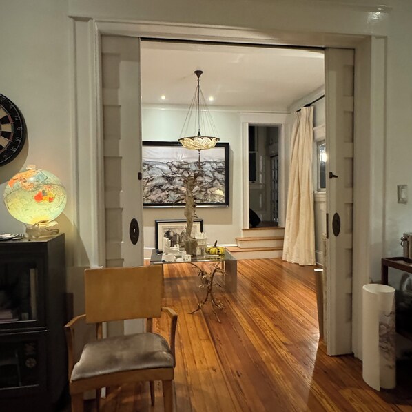 A room with a wooden floor, a desk with a lamp, a chair, and a painting on the wall.