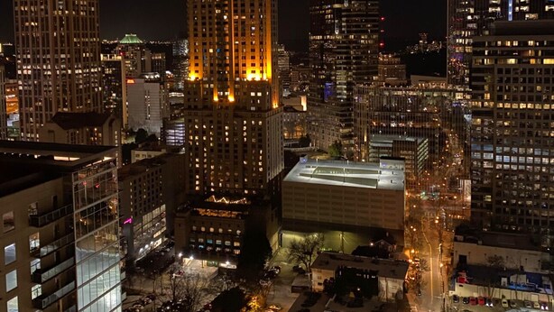 A nighttime cityscape with illuminated skyscrapers and a parking lot.