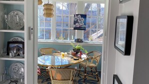 A dining area with a round table, wicker chairs, and a view through large windows.