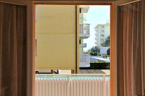 Vista de um quarto com porta de correr para uma varanda externa. A varanda possui grade branca e uma pequena piscina.