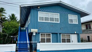 A two-story blue house with a white door, a small porch, and a blue gate. - Right between Guyana’s famous malls, family sized condo with safe neighborhood (Georgetown)