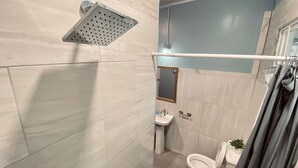 A bathroom with a shower, toilet, sink, and a mirror. - Right between Guyana’s famous malls, family sized condo with safe neighborhood (Georgetown)