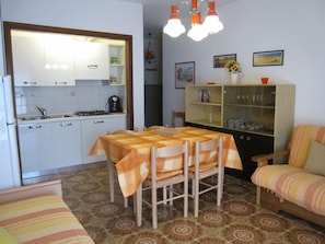 Une cuisine de taille réduite avec des meubles blancs, une table à manger recouverte d’une nappe à carreaux et un canapé agrémenté de coussins à rayures.