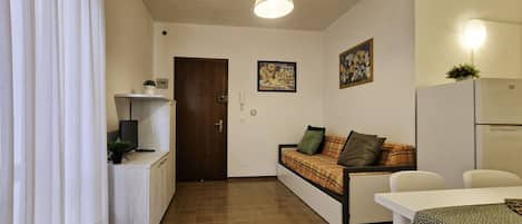 Un espacio habitable compacto con kitchenette, sofá, mesa de comedor y refrigerador.