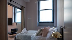 Ett sovrum med en säng, en stol, en lampa och två fönster.