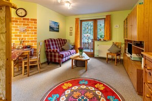 A cozy living room with a brick wall, a red plaid sofa, a wooden coffee table, and a view through a glass door.