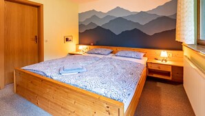 A bedroom with a bed, wooden headboard, nightstands, a wall mural, and a window with a curtain.