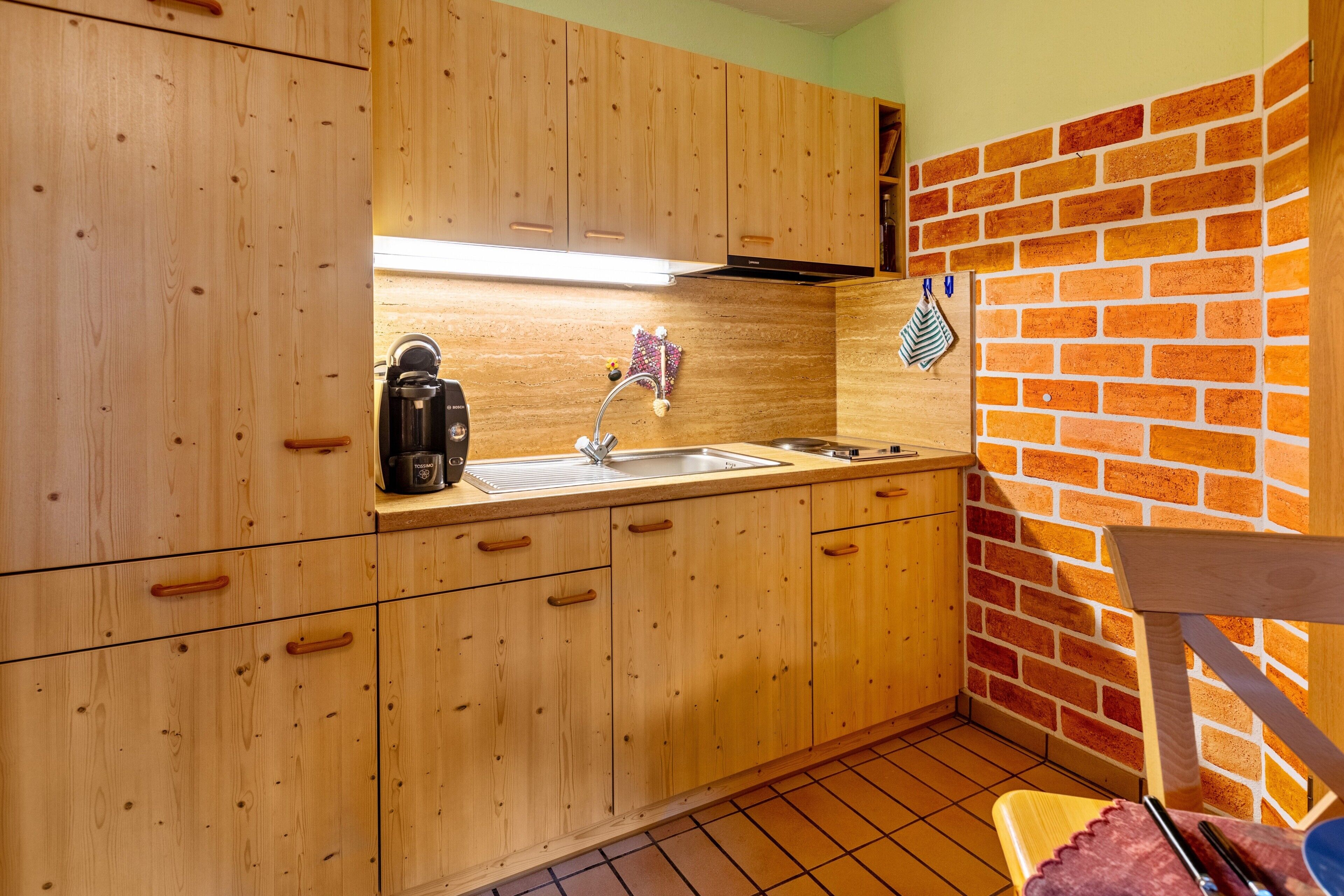 A kitchen with wooden cabinets, a sink, a coffee maker, and a brick wall.