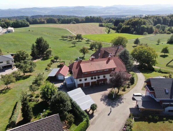 A large building with a red-tiled roof, surrounded by green fields and trees.