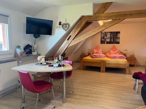 Une pièce comprenant un lit, un téléviseur, une table à manger avec des chaises et une structure de plafond en bois.