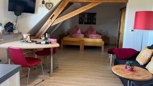 Ein gemütliches Loft-Zimmer mit Holzbalkendecke, einem Bett mit roter Bettwäsche, einem Essbereich mit roten Stühlen und einem an der Wand montierten Fernseher.