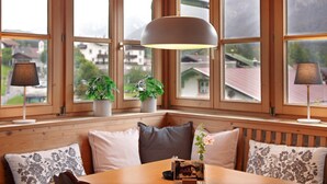 A room with large windows, a wooden bench, and a table with a lamp. - Apartment 'Kramernest' with Mountain View, Balcony and Wi-Fi (Grainau)