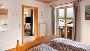 A bedroom with a wooden headboard, a window with curtains, a radiator, and a view of the outside. - Apartment 'Kramernest' with Mountain View, Balcony and Wi-Fi (Grainau)