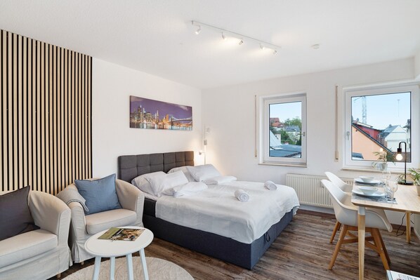 Un dormitorio moderno con una cama, un sofá, una mesa de comedor y un cuadro de un paisaje urbano.
