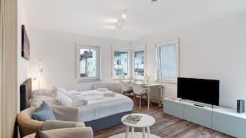 Ein modernes Schlafzimmer mit Bett, Schreibtisch, Fernseher und Blick auf die Stadt.