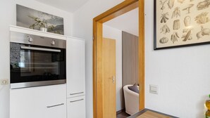 Une cuisine moderne dotée d’un four encastré et d’une porte en bois donnant sur une pièce dont un des murs est à rayures.