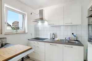 Una cocina moderna con armarios blancos, un lavamanos de acero inoxidable y una ventana con vista a un edificio.