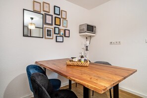 A dining area with a wooden table, two chairs, a woven basket with bottles, a wall-mounted TV, and framed pictures.