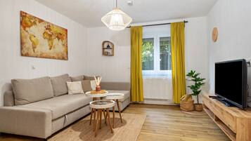 Ein Wohnzimmer mit einer Couch, einem Fernseher, einem Wandbild einer Weltkarte, einer Pendelleuchte und einem Fenster mit gelben Vorhängen.