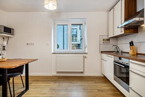 A modern kitchen with a wooden table, built-in oven, and a window with a view of buildings.