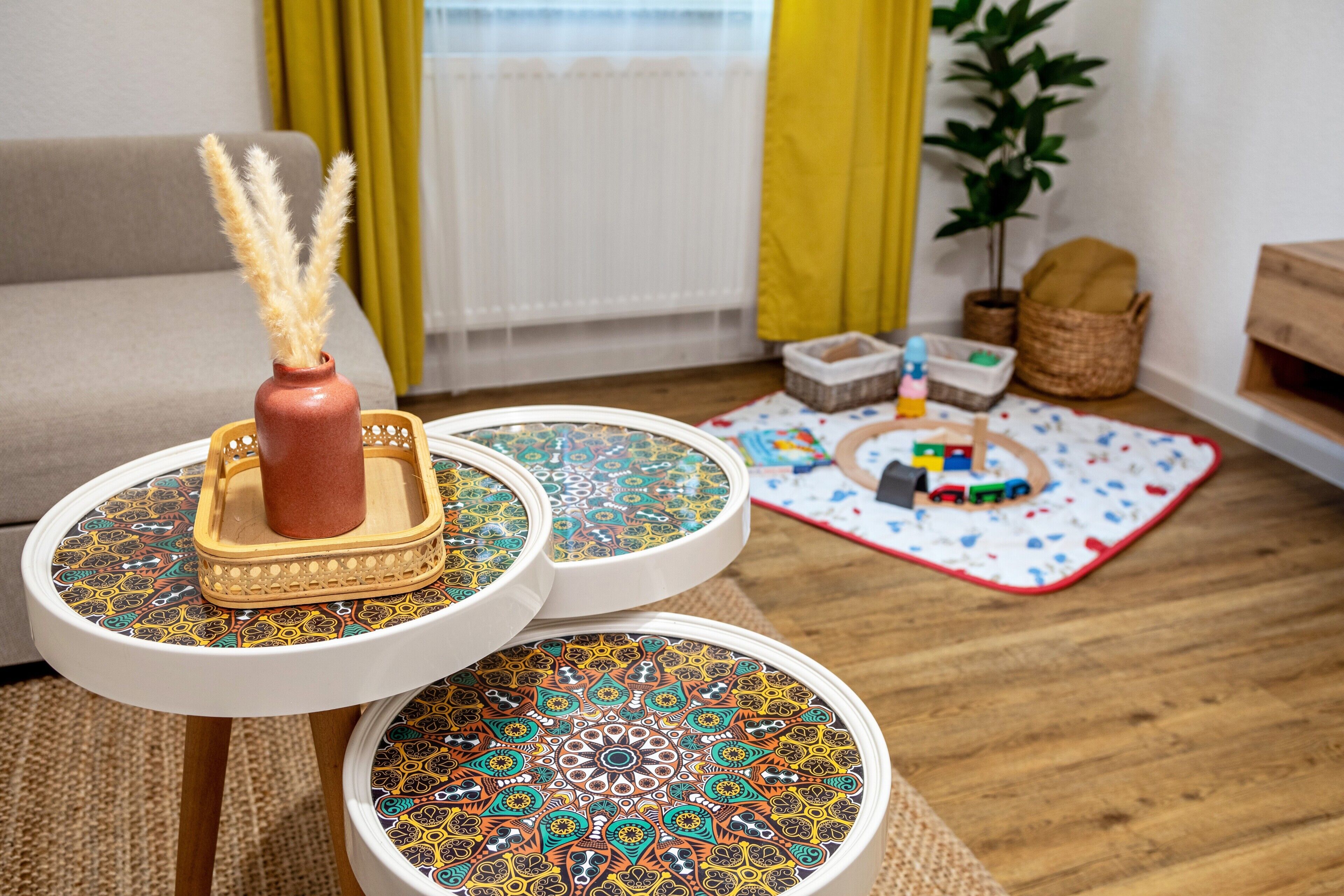Ein Wohnzimmer mit einer Couch, einem kleinen Tisch mit einer dekorativen Vase, einer gemusterten Ablage und einer Spielmatte auf dem Boden.