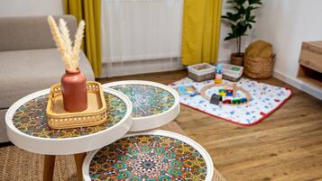 Ein Wohnzimmer mit einer Couch, einem kleinen Tisch mit einer dekorativen Vase, einer gemusterten Ablage und einer Spielmatte auf dem Boden.