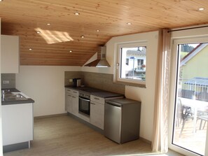 A modern kitchen with wooden ceiling, built-in appliances, and a large window.