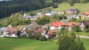 Eine Wohngegend mit Häusern, einige mit Solaranlagen, umgeben von Grünflächen und Hügeln.