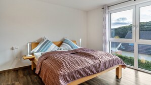 Ein Schlafzimmer mit Bett, Nachttisch und einem Fenster mit Blick auf Gebäude und Bäume.