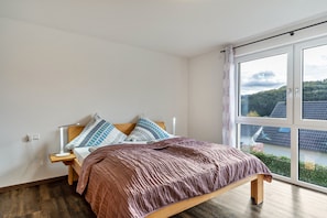 Une chambre à coucher avec un lit, une table de chevet et une fenêtre donnant sur des immeubles et des arbres.