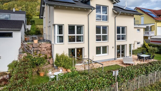 Ein zweistöckiges Haus mit Solaranlage, einer Steintreppe, einer Terrasse mit Gartenmöbeln und einem umzäunten Garten.