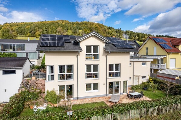 Une maison moderne à deux étages, dotée de panneaux solaires, d’un escalier en pierre et d’un jardin bien entretenu.