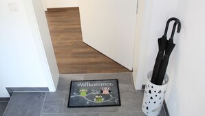 Un pasillo con piso de madera, un felpudo con lechuzas y un portalmangas blanco.