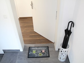 Un couloir avec un plancher en bois, un paillasson orné de motifs de hiboux et un porte-parapluie blanc.