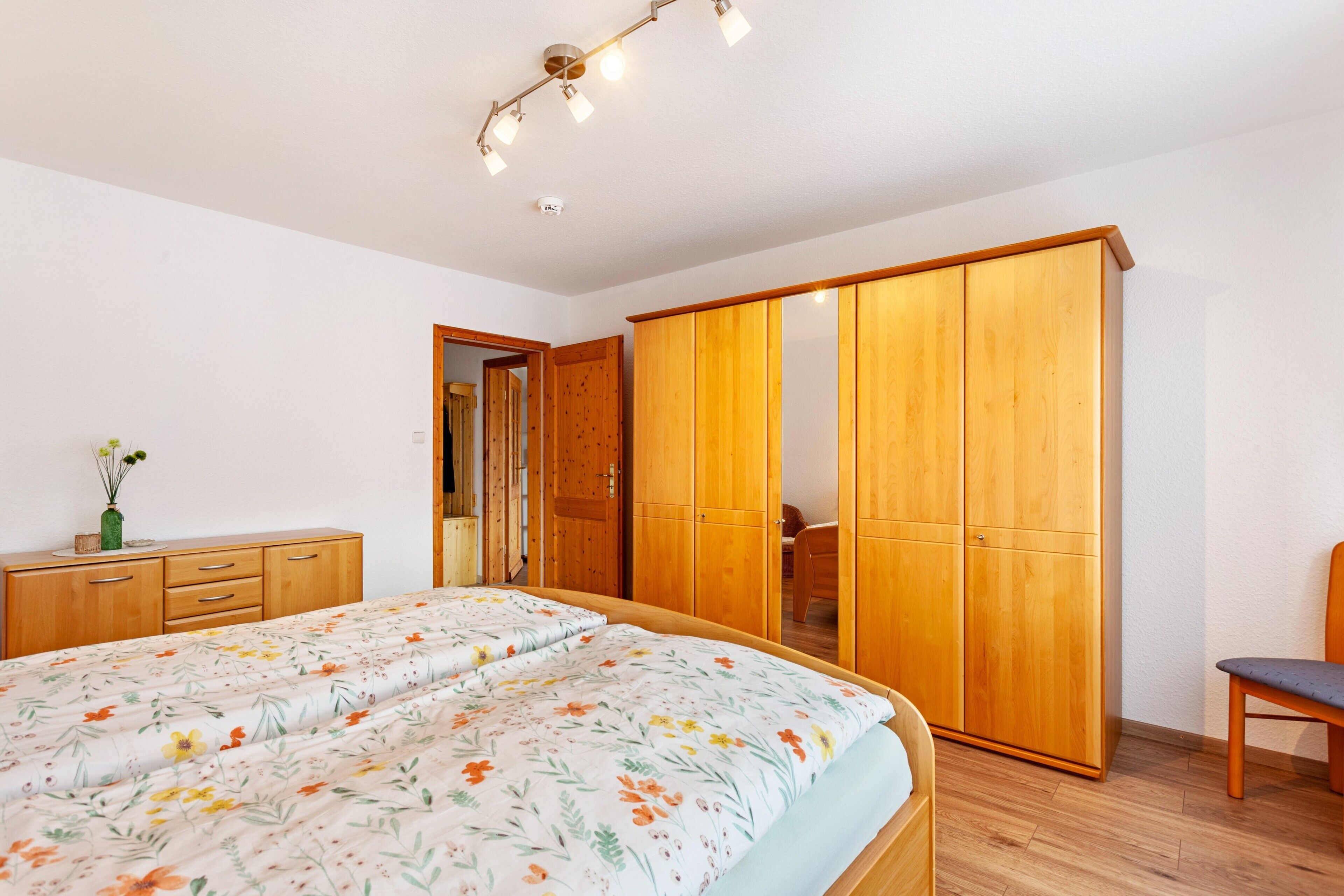 A bedroom with a bed, wooden wardrobe, and a chair.