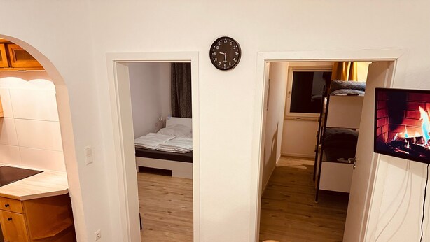 Una habitación con una cama, un escritorio, una silla, un televisor y un reloj en la pared.