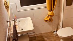 Un baño con lavamanos, inodoro y ventana con cortinas.
