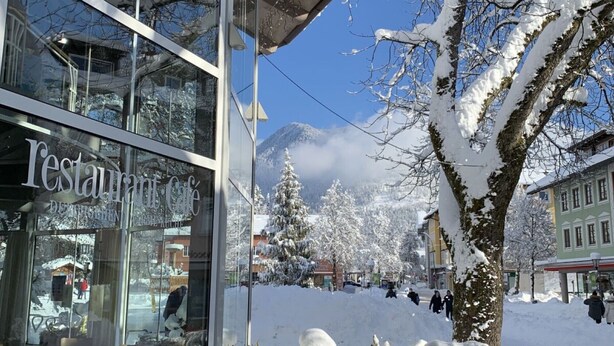 Ein Restaurant mit Glasfassade, schneebedeckten Bäumen und einer Bergkulisse im Hintergrund.