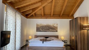 Ein Schlafzimmer mit Holzboden, einem Bett mit weißer Bettwäsche, einem an der Wand befestigten Fernseher und einem großen Landschaftsbild.