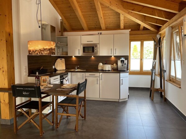 A modern kitchen with white cabinets, a wooden ceiling, and a dining area with a table and chairs.