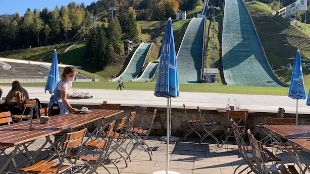 Terrasse mit Tischen und Stühlen, im Hintergrund Berge und eine Seilbahn.
