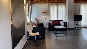 Ein Wohnzimmer mit einem dunklen Sofa, einem weißen Sessel, einem Couchtisch, einem Fernseher und einer Stehlampe.