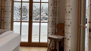Una habitación con cama, una silla y vistas a un paisaje nevado a través de un ventanal.