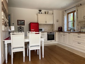 A kitchen with white cabinetry, a red appliance, and a dining area with white chairs. - Apartment 'Ferienwohnung Max 3' with Mountain View, Private Terrace and Wi-Fi (Garmisch-Partenkirchen)